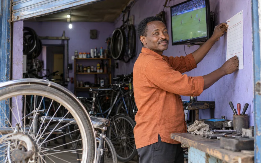 Tanzania sports information scene with an adult in a bicycle workshop beside a football screen and coupon