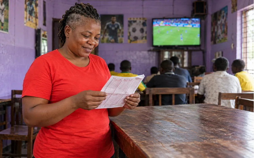 Wasafi Bet jackpot coupon reading illustrated by an adult with a multi-match sheet in a supporters room