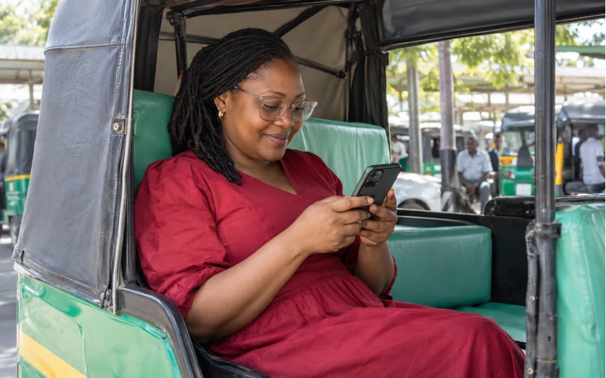 Wasafi Bet login guidance illustrated by an adult passenger checking her own phone in a stationary bajaji