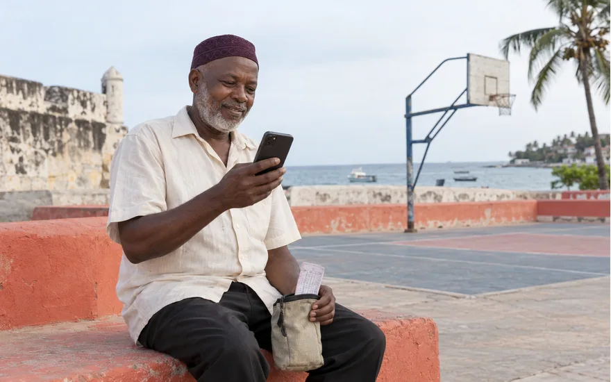 Adult Tanzania account holder with a phone and folded sports coupon beside a quiet basketball court