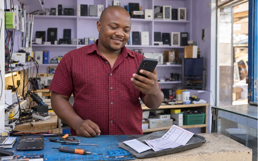 Adult Tanzania phone owner at an electronics bench with a private SIM envelope and football coupon