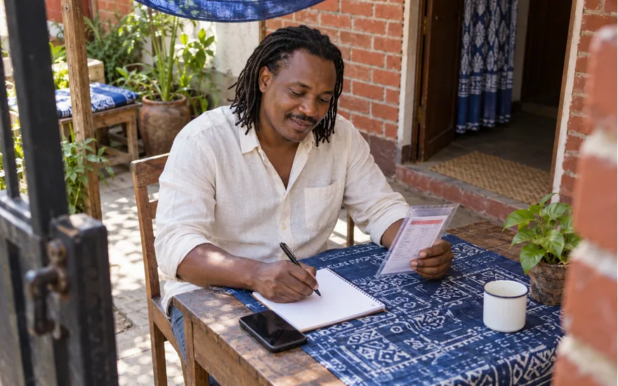 Adult Tanzania reader organising a sports ticket, phone and case notes in a residential courtyard