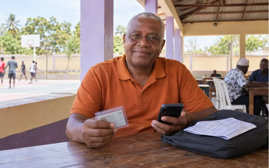 Adult Tanzania account-checking scene with an unreadable identity sleeve and phone in a quiet community hall
